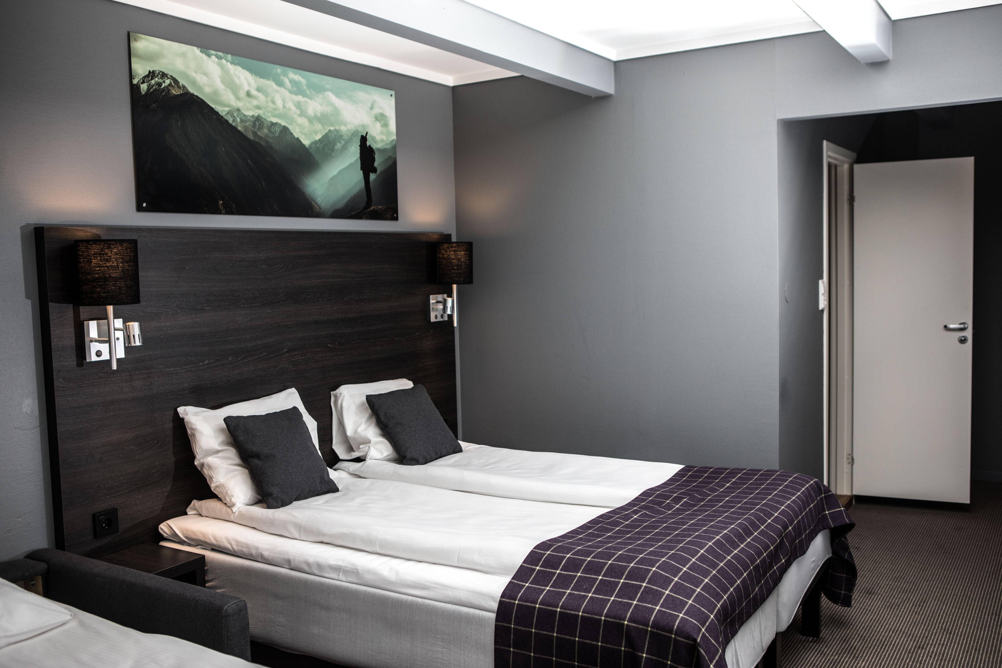 A hotel room with a bed, two bedside tables, a headboard, a wall-mounted artwork, and a door.