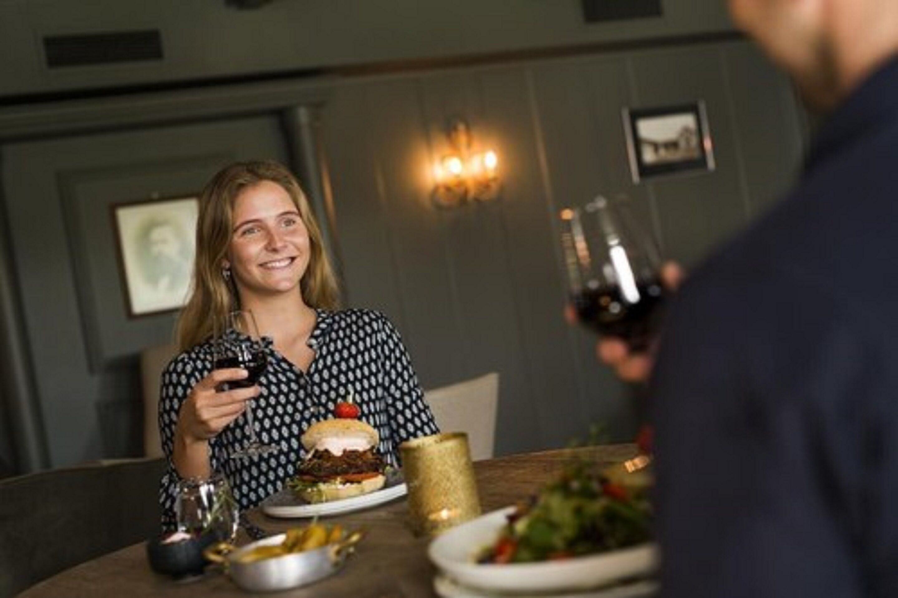 A dining table with a burger, salad, and wine glasses.