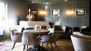 A modern lounge area with a round table, several armchairs, and a piano.