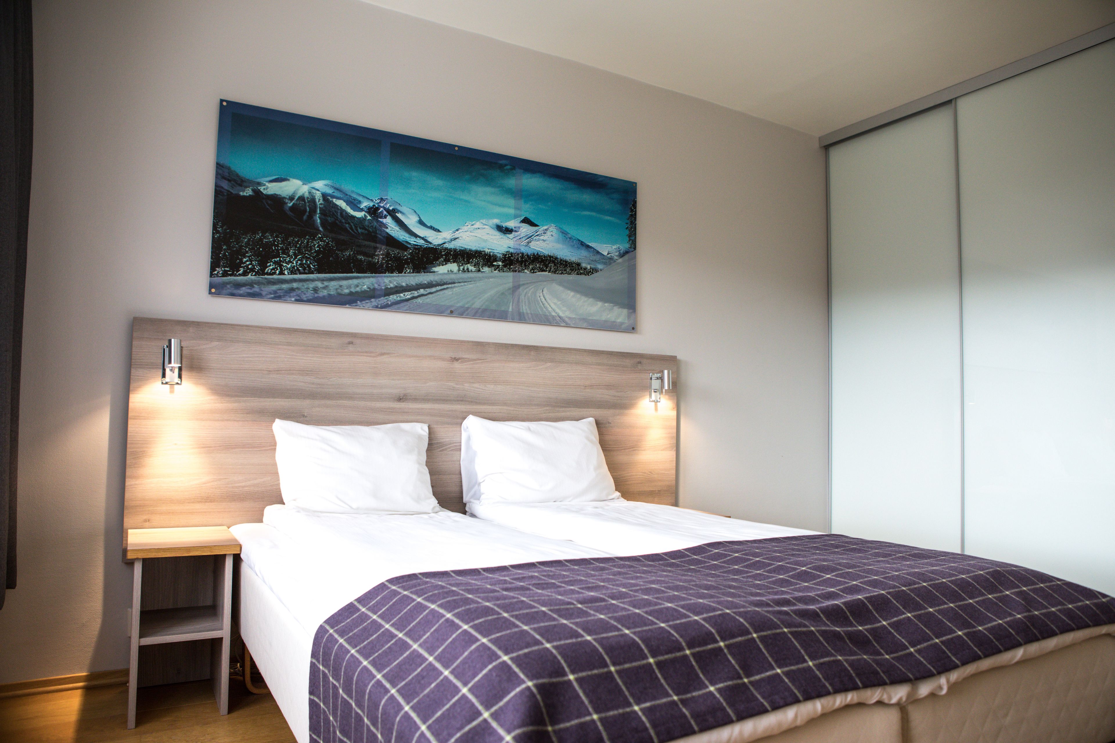 A bedroom with a bed, a nightstand, a wall-mounted painting, and a sliding closet door.