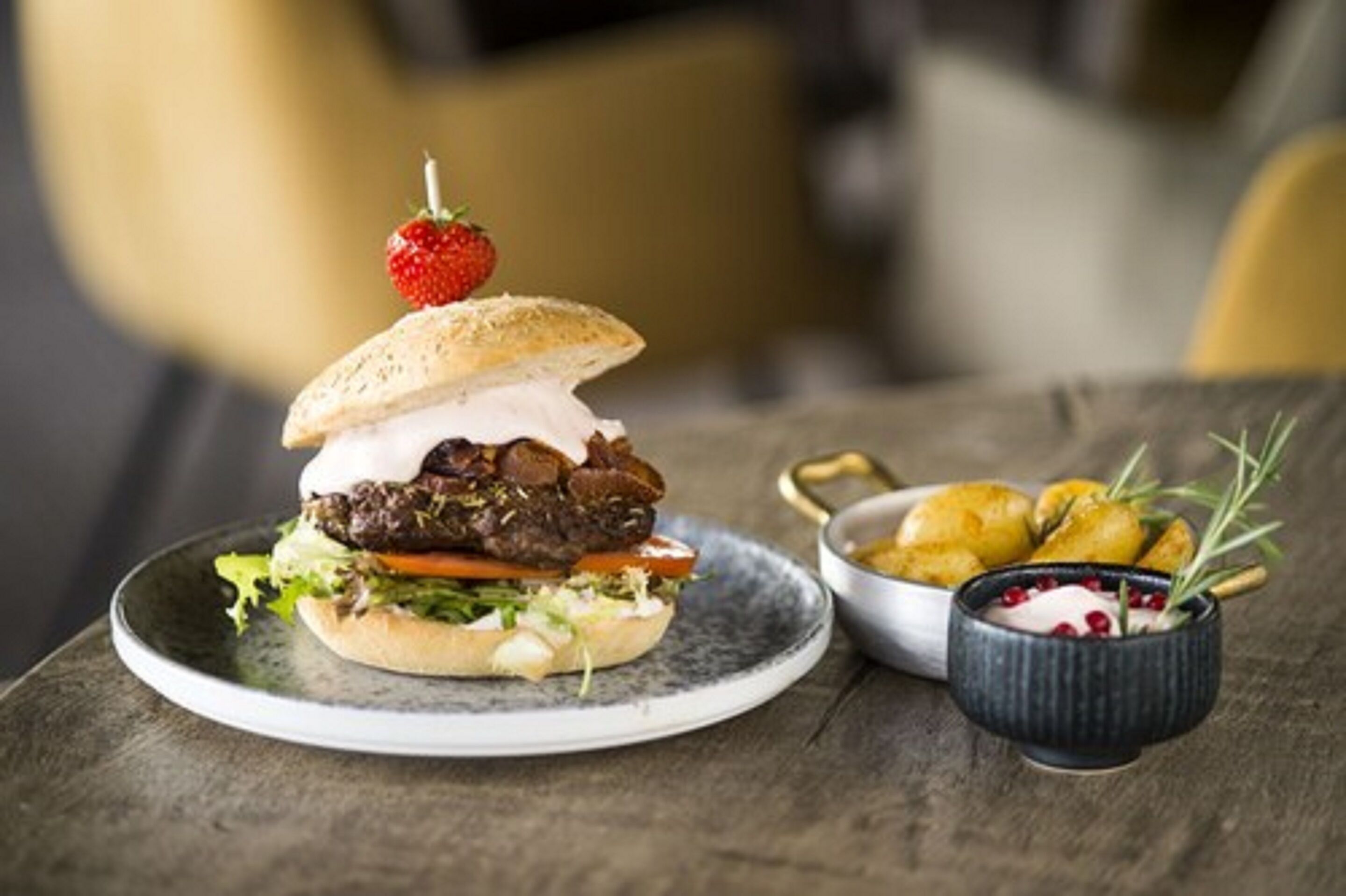 Hamburguesa con fresa encima, acompañada de patatas asadas y un pequeño recipiente de salsa.