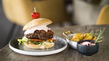 Hamburguesa con fresa encima, acompañada de patatas asadas y un pequeño recipiente de salsa.
