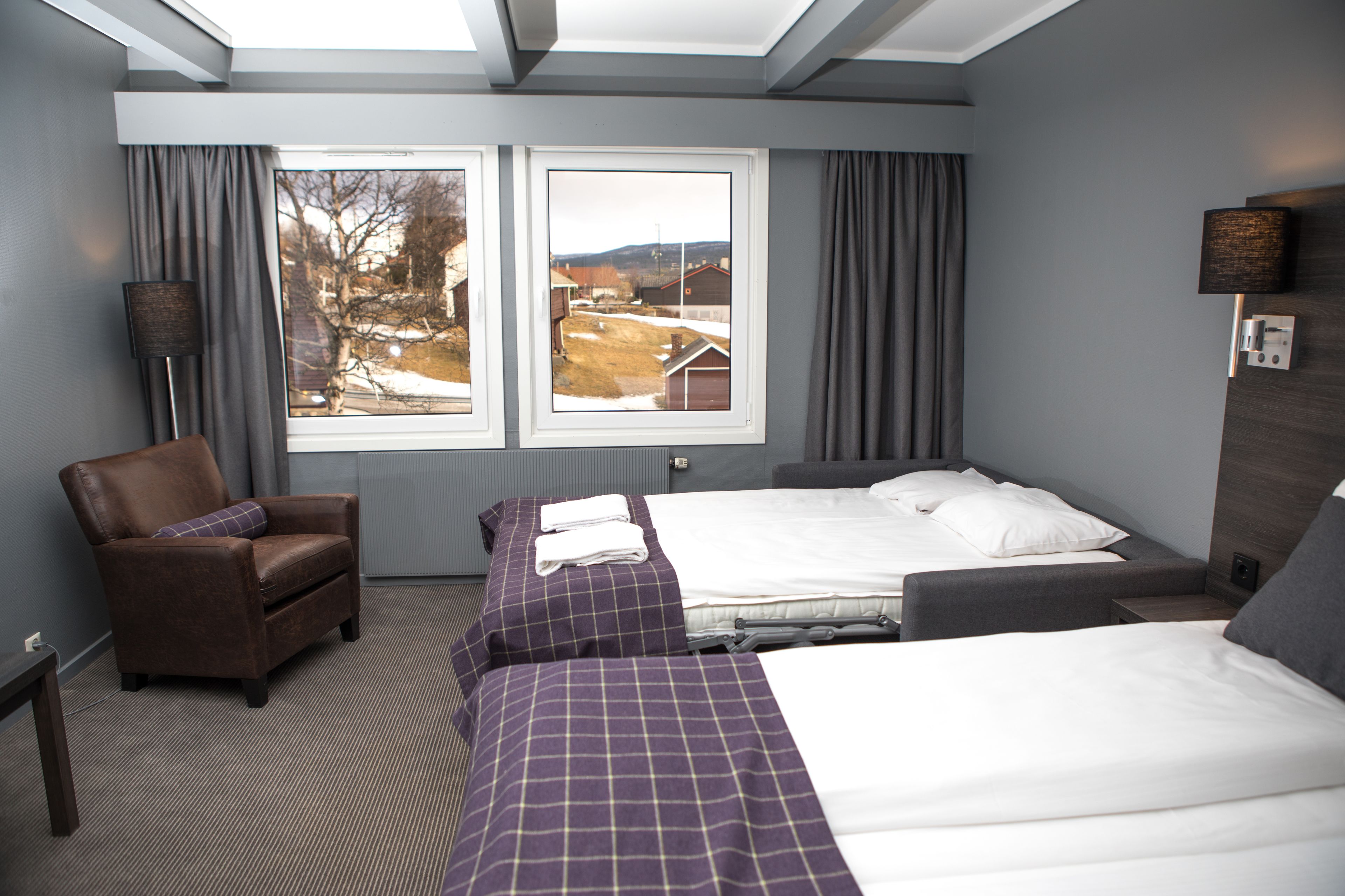 A hotel room with two beds, a chair, a window with a view of a snowy landscape, and a lamp.