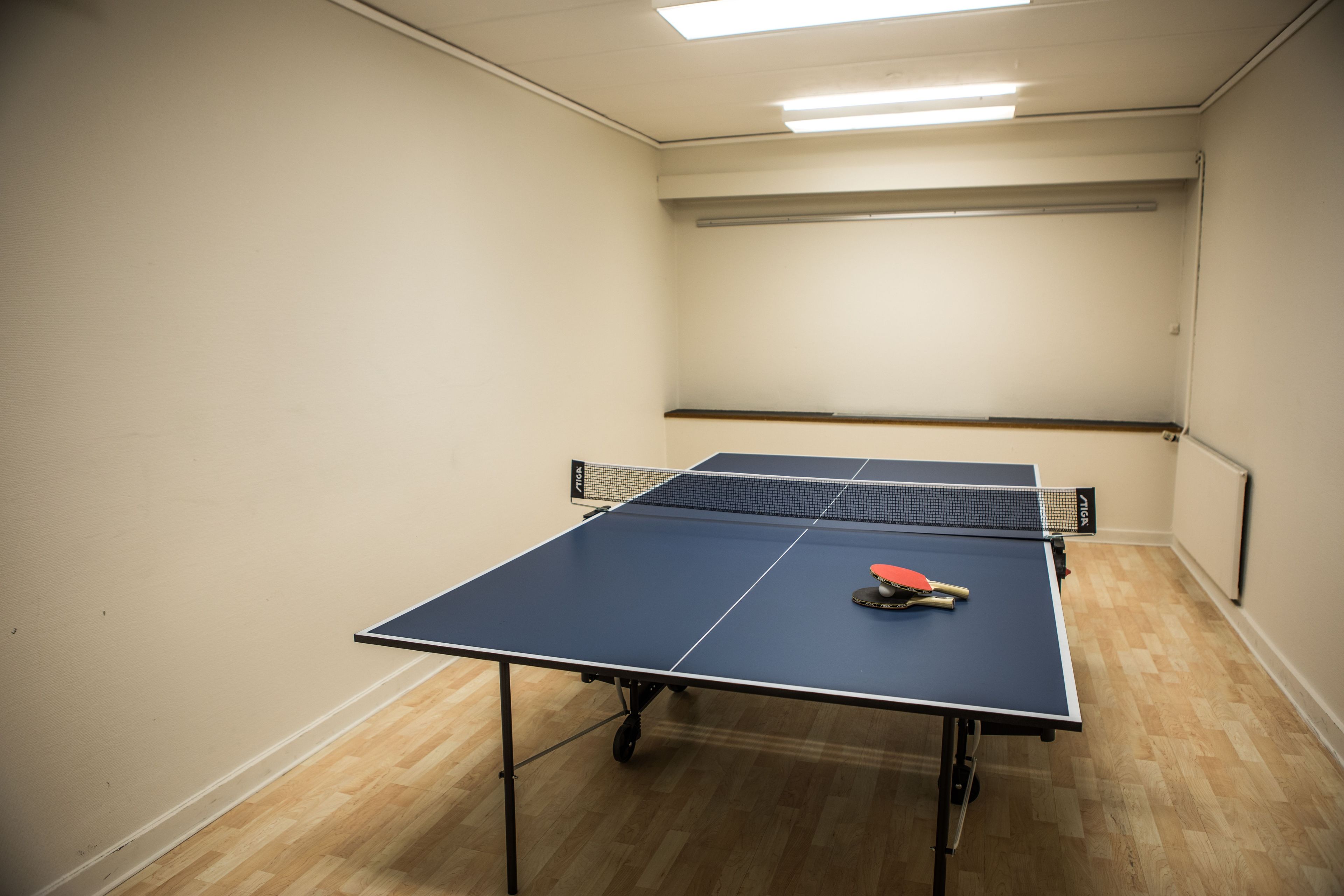 Una mesa de ping pong en una habitación con suelo de madera y paredes blancas.