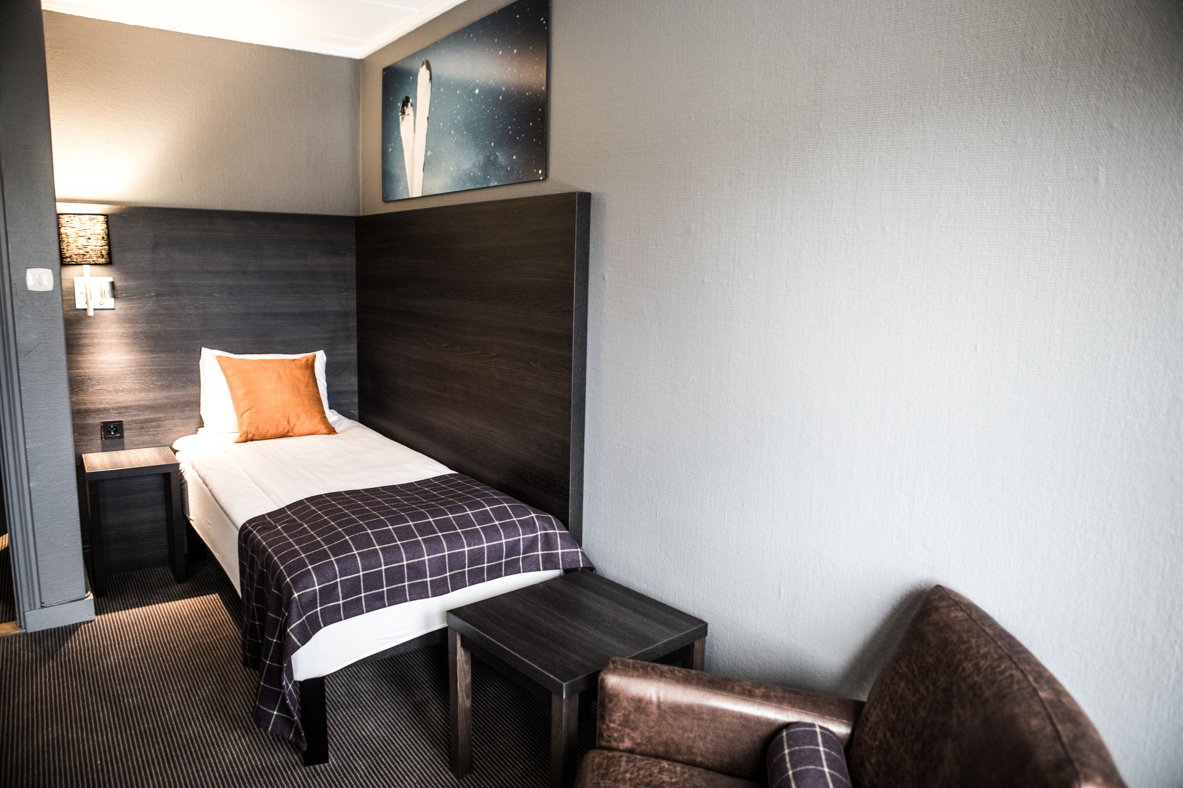 Una habitación de hotel con cama, mesita de noche, una silla y una obra de arte colgada en la pared.