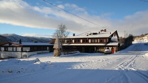A snow-covered building with a sloped roof, a stone pillar, and a car parked in front.