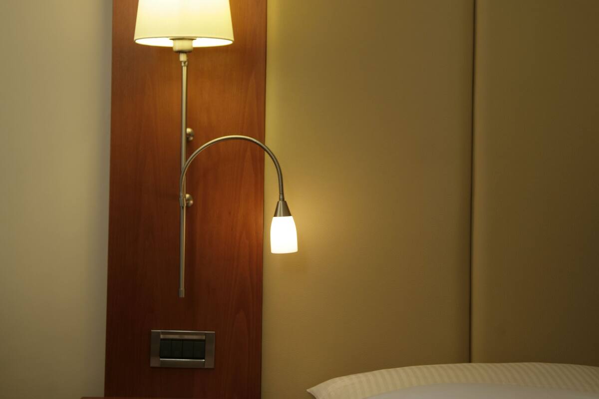 Una habitación de hotel con una lámpara de noche, una mesita y una cama.