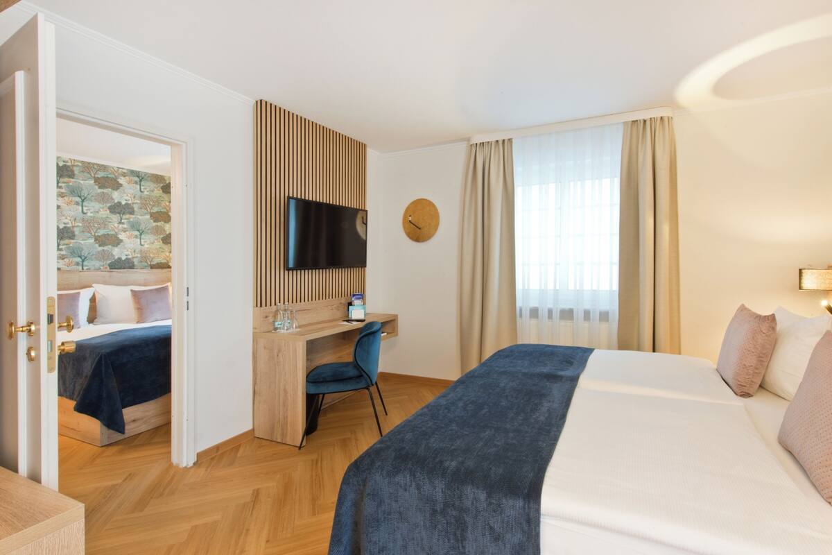 Habitación de hotel con cama, escritorio, silla, televisor y un reloj en la pared.