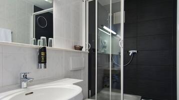 Un baño moderno con lavamanos blanco, inodoro y cabina de ducha con mampara de vidrio.