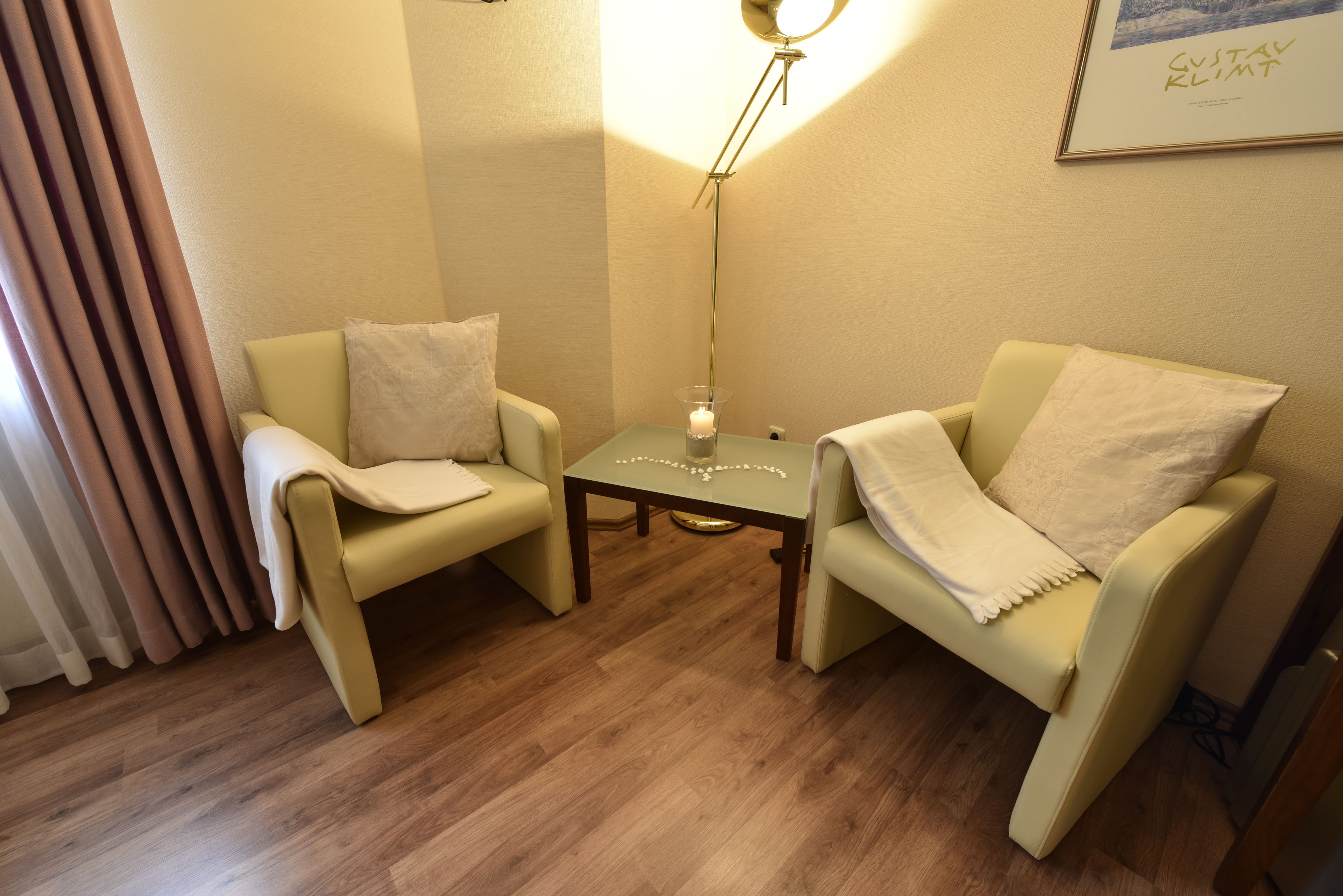 Una habitación con dos sillones color beige, una mesita con una vela y un cuadro enmarcado en la pared.