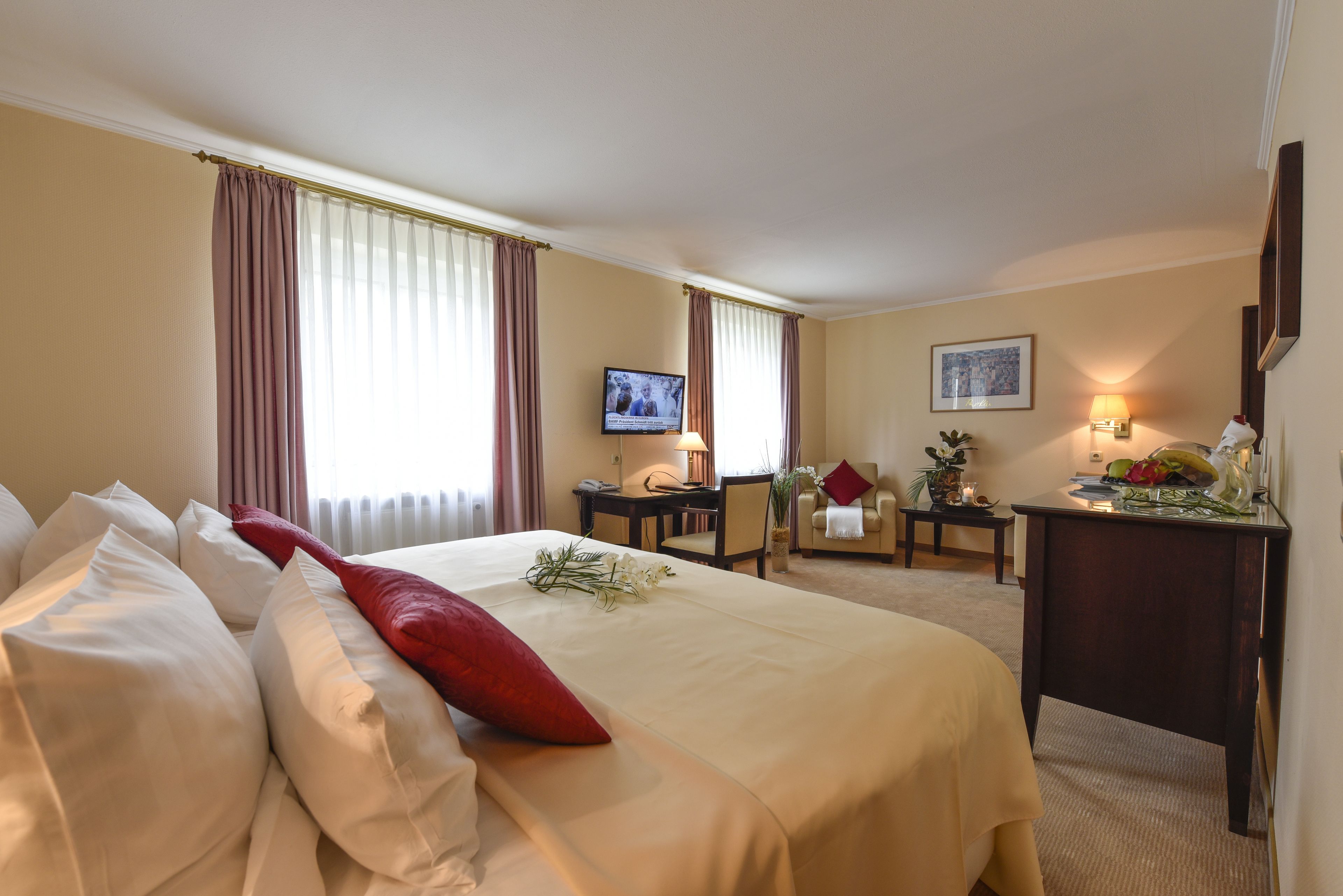 Ein Hotelzimmer mit einem großen Bett, einem Schreibtisch, einem Sessel, einem Fernseher und einer Lampe.