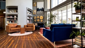 A modern living room with a wooden floor, leather armchairs, a blue sofa, and a bookshelf filled with books and decorative items. - Atrium Hotel Amadeus (Osterfeld)