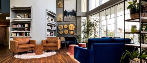 Una sala de estar moderna con piso de madera, sillones de cuero, un sofá azul y una estantería llena de libros y objetos decorativos.