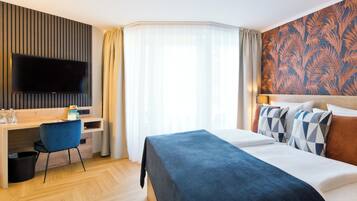 Habitación de hotel con cama, escritorio, silla, televisor y ventana con cortinas.