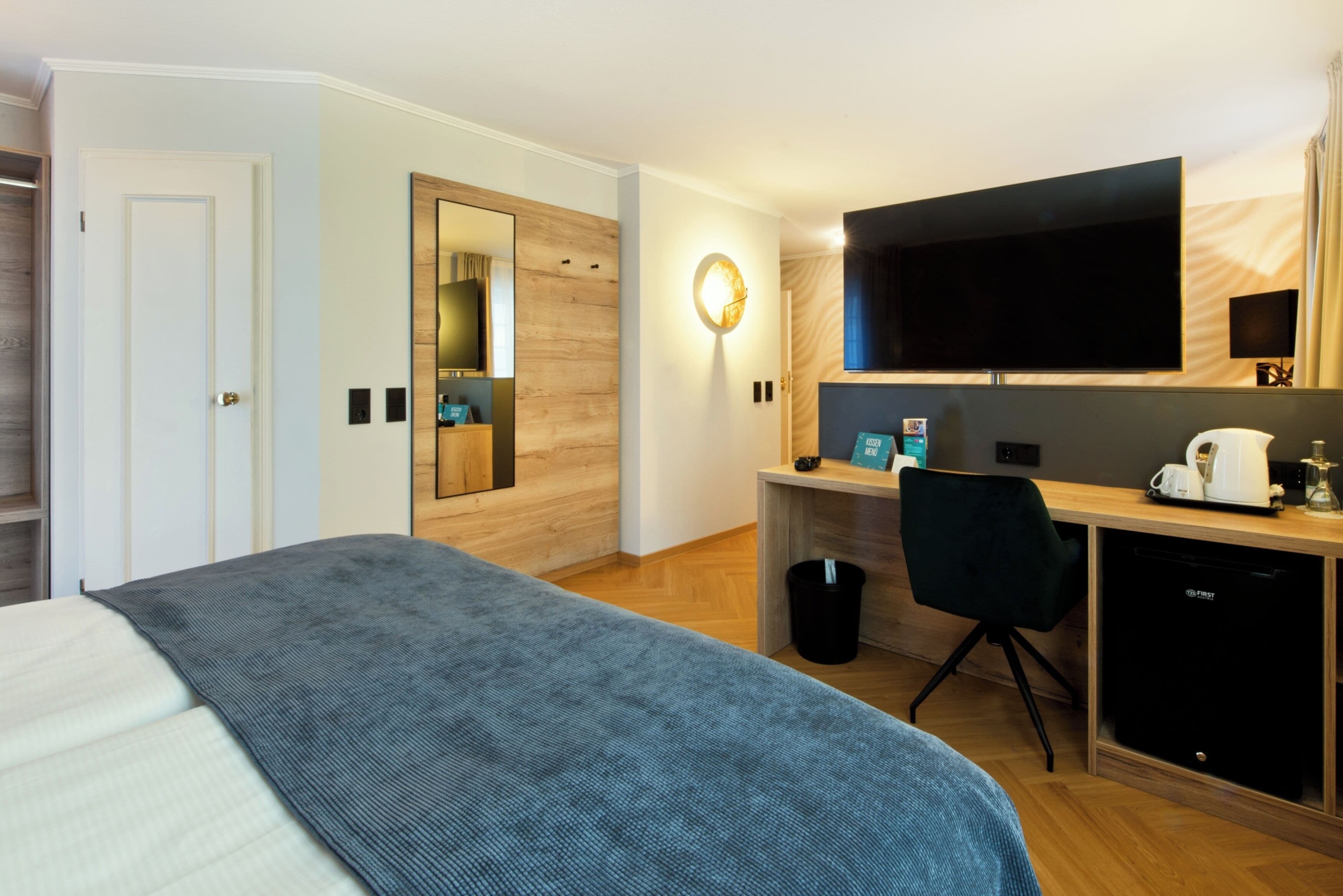 A hotel room with a bed, a desk with a computer, a television, and a coffee machine.