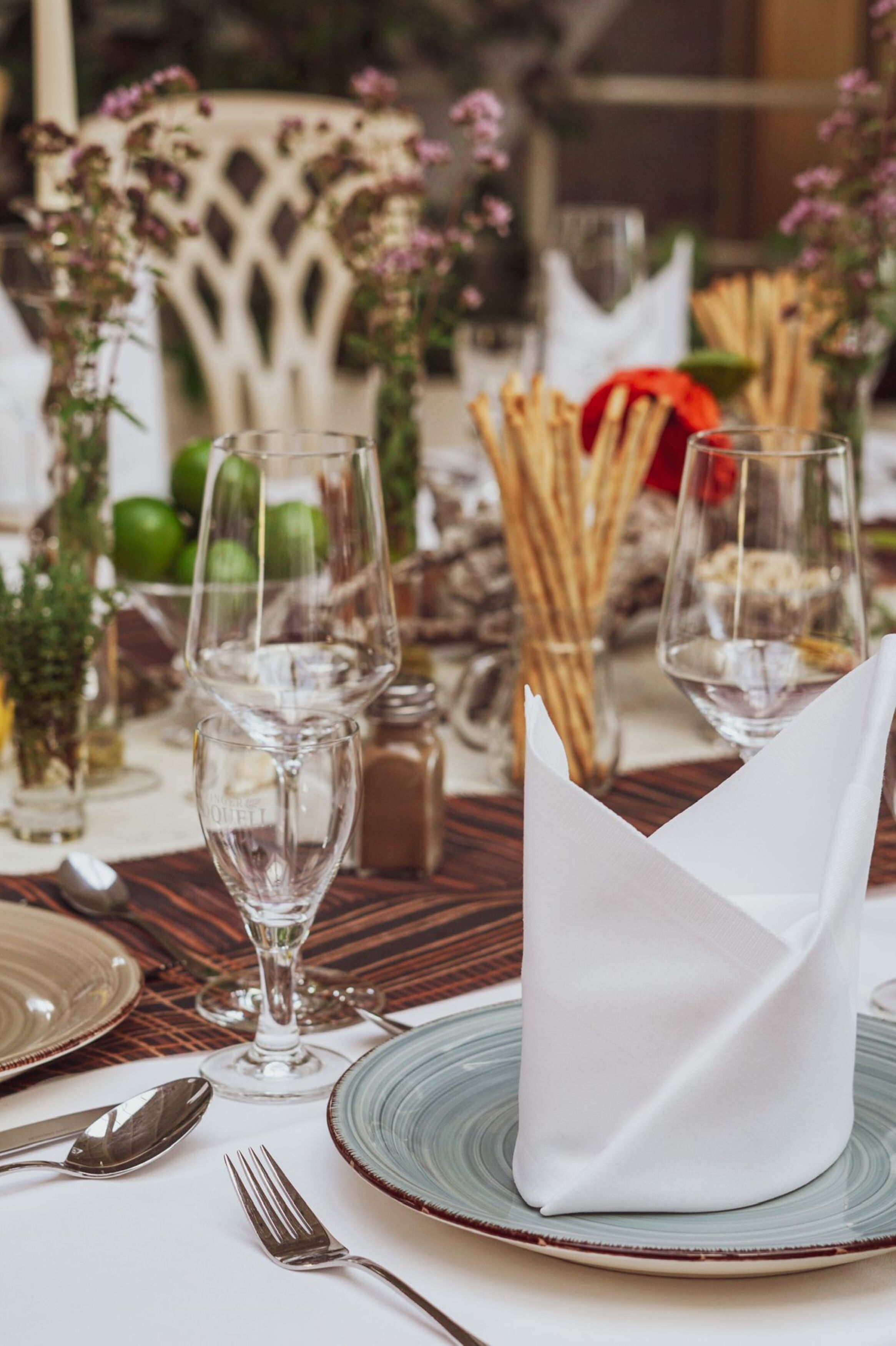 Una mesa servida con copas de vino, platos y cubiertos, con un servilleta doblada sobre el plato.