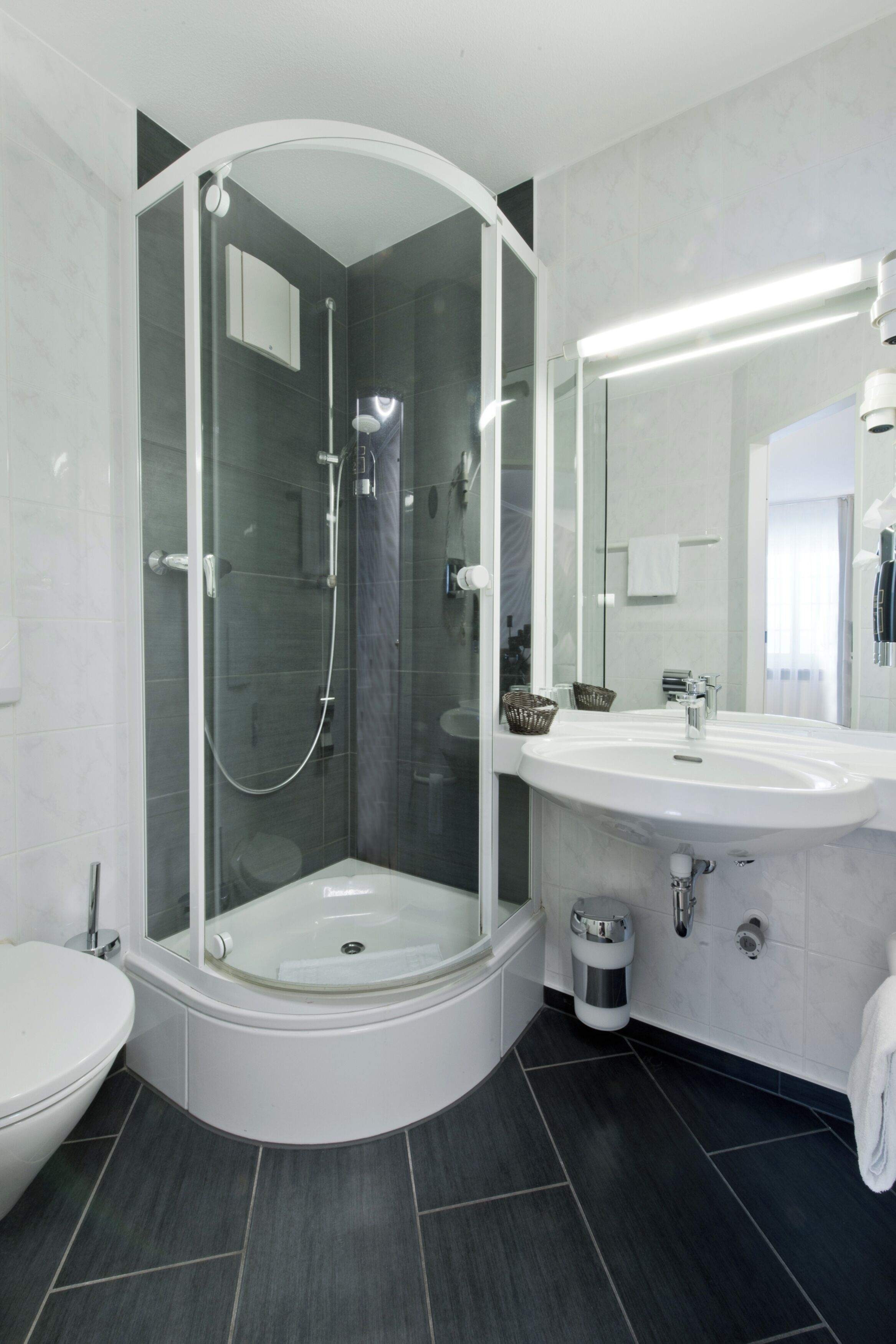 Un baño moderno con ducha envuelta en vidrio, un lavamanos blanco y un espejo grande.