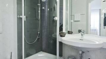 Un baño moderno con ducha envuelta en vidrio, un lavamanos blanco y un espejo grande.