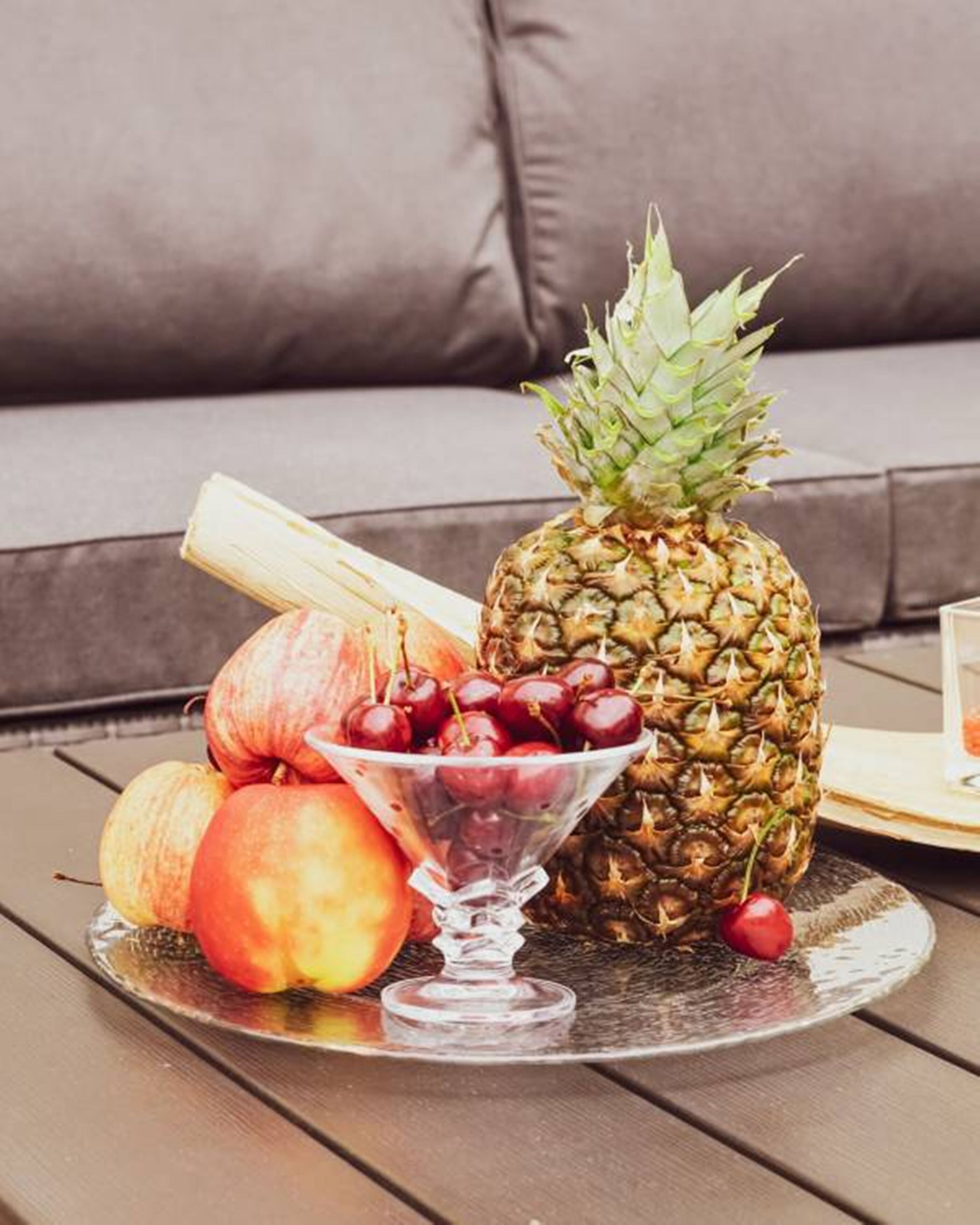 A fruit platter with a pineapple, cherries, and peaches on a wooden table.