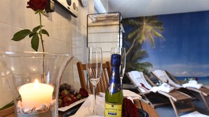 A table with a candle, champagne bottle, and glasses, set against a backdrop of a beach scene mural. - Atrium Hotel Amadeus (Osterfeld)