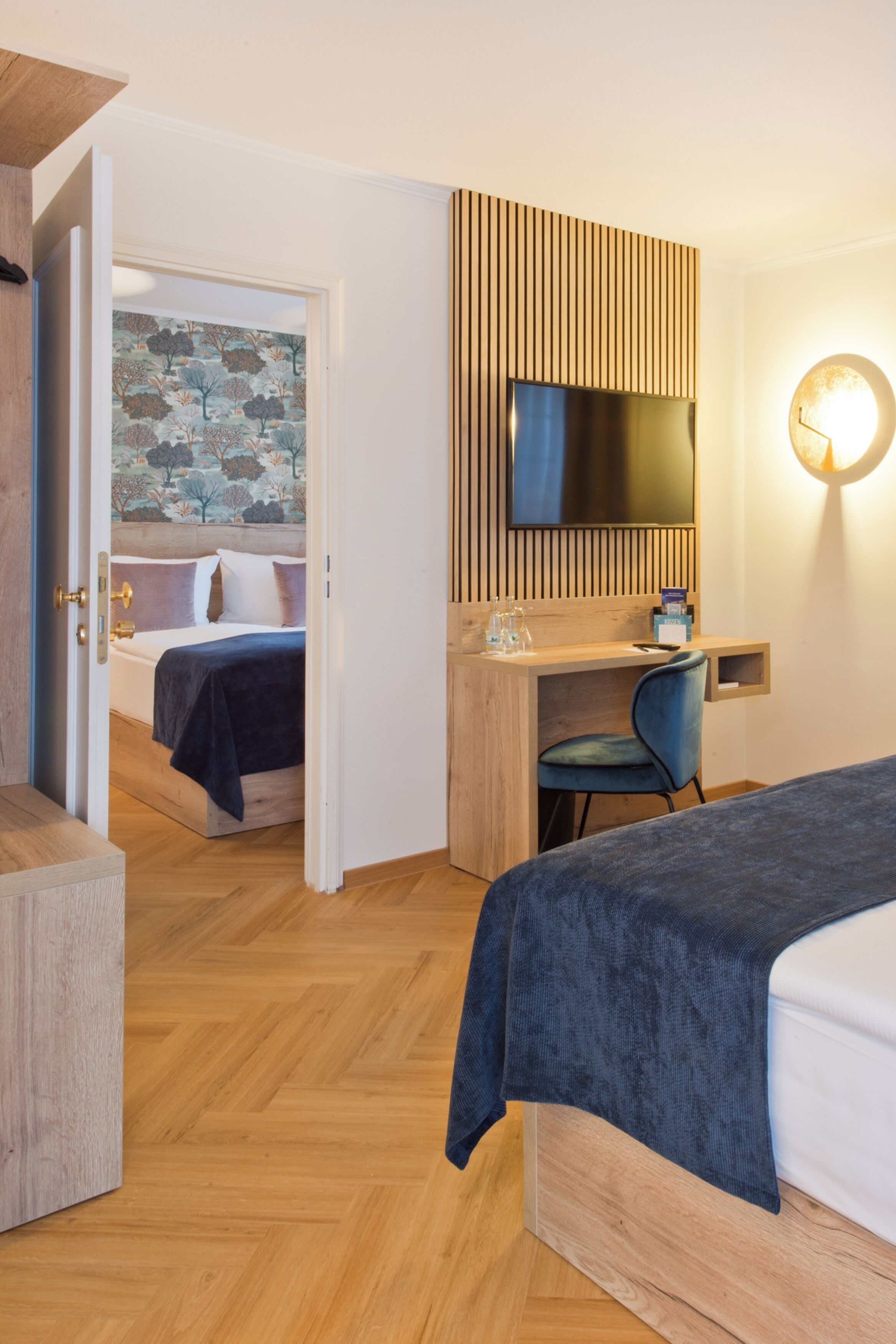 Ein Hotelzimmer mit einem Bett, einem Schreibtisch mit Stuhl, einem Fernseher und einer Wandleuchte.