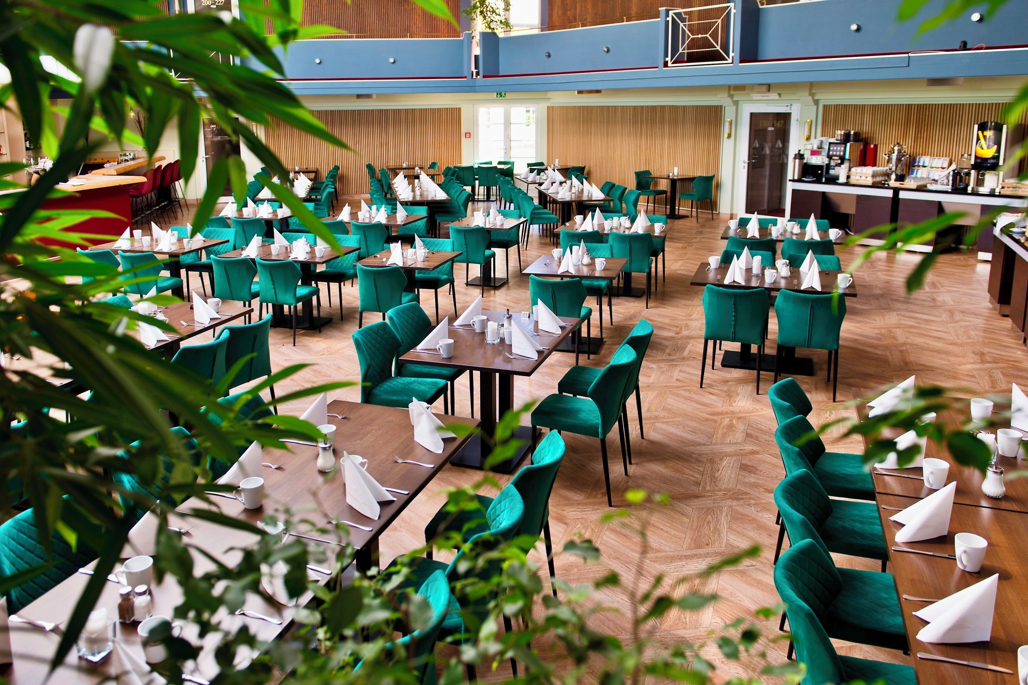 Un grand espace dédié à la salle à manger, avec plusieurs tables et chaises, une cuisine à l’arrière-plan et un plancher en bois.