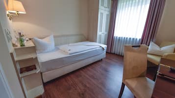 A hotel room with a bed, a chair, a desk, a lamp, and a wardrobe.