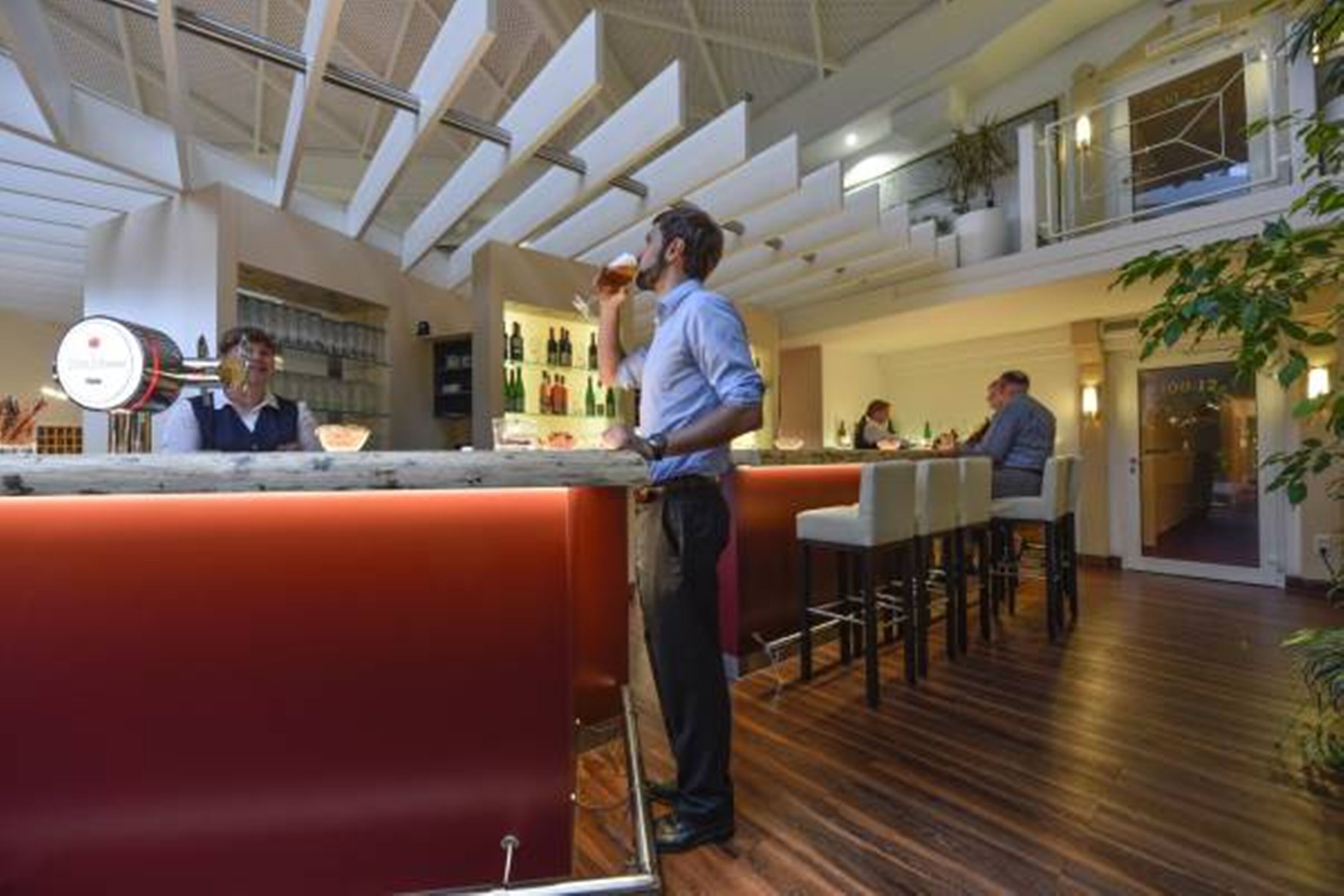 Een moderne bar met een hoge plafond, houten vloer en een bar achter met krukken.