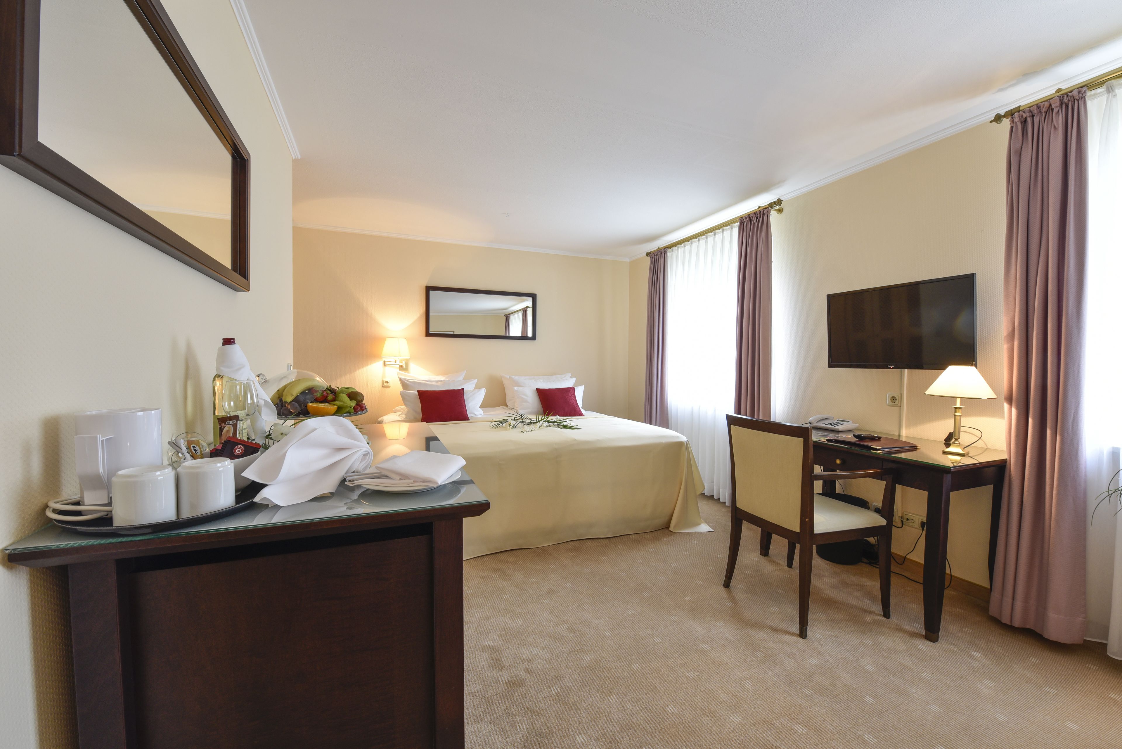 Habitación de hotel con cama, escritorio, silla, televisor y zona de comedor con mesa y sillas.