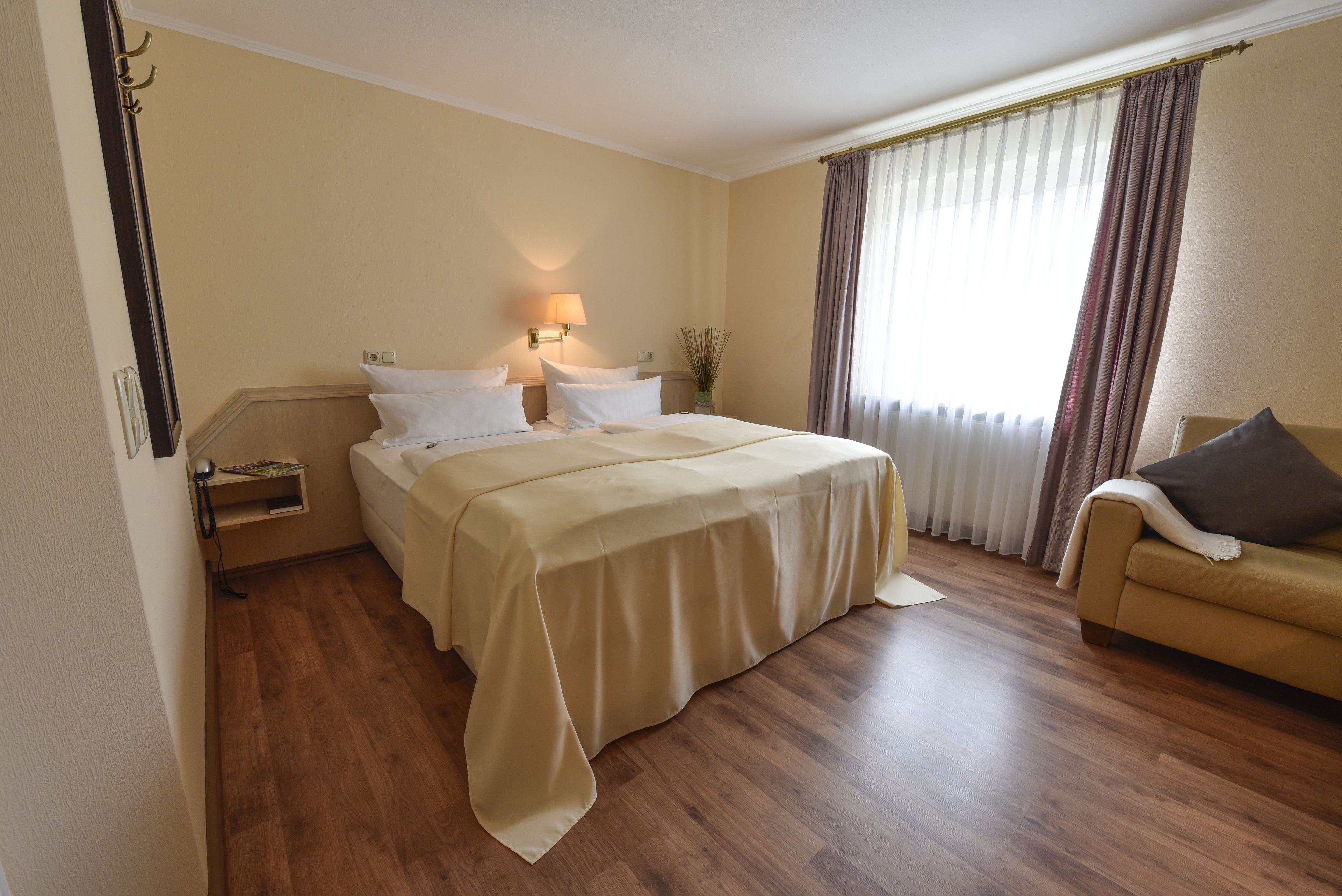 Una habitación de hotel con cama, mesitas de noche, lámpara, sofá y ventana con cortinas.