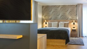 A modern hotel room with a large bed, wooden headboard, and a flat-screen TV mounted on a wall. - Atrium Hotel Amadeus (Osterfeld)