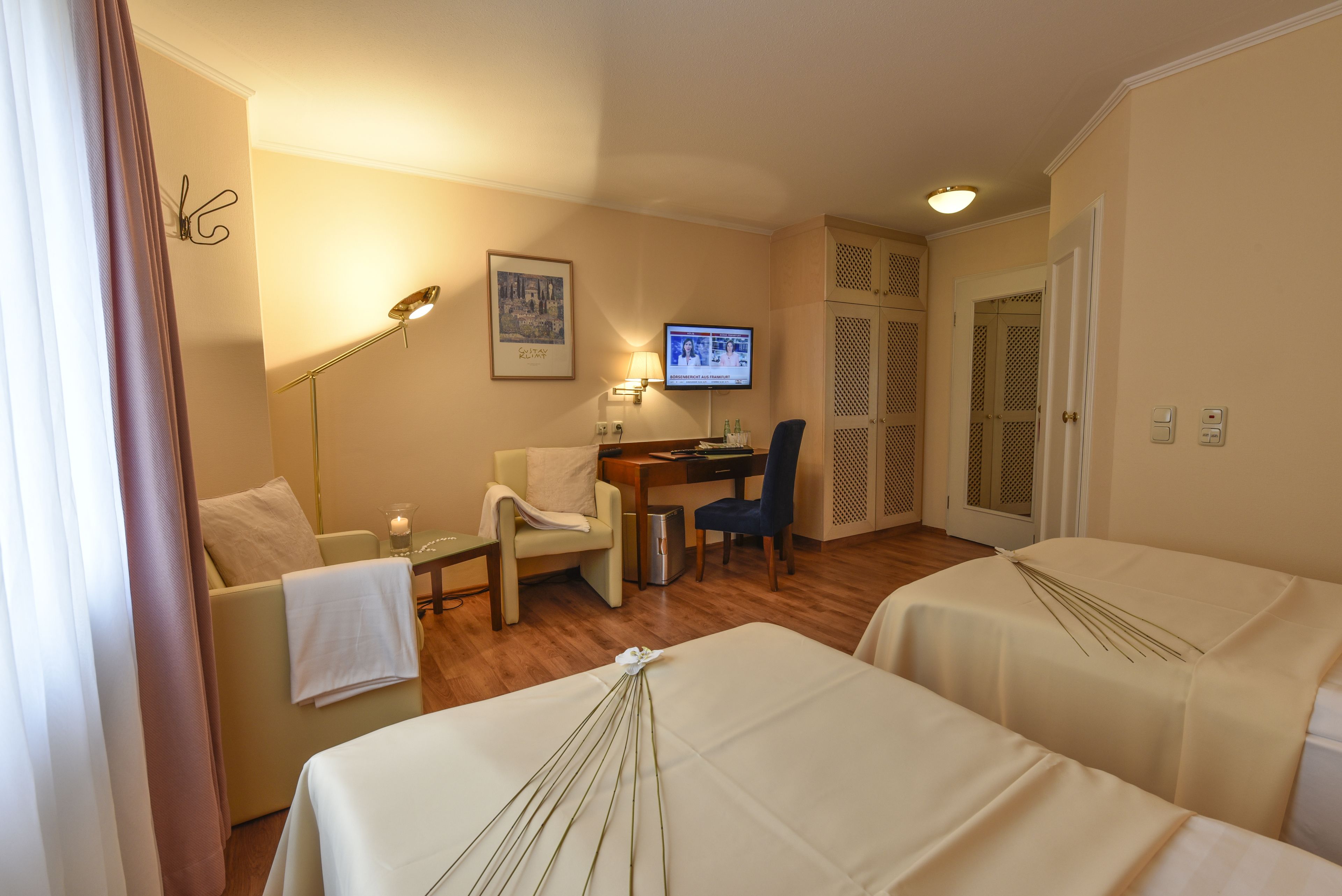 Ein Hotelzimmer mit zwei Betten, einem Schreibtisch, einem Stuhl, einem Fernseher und einer Lampe.