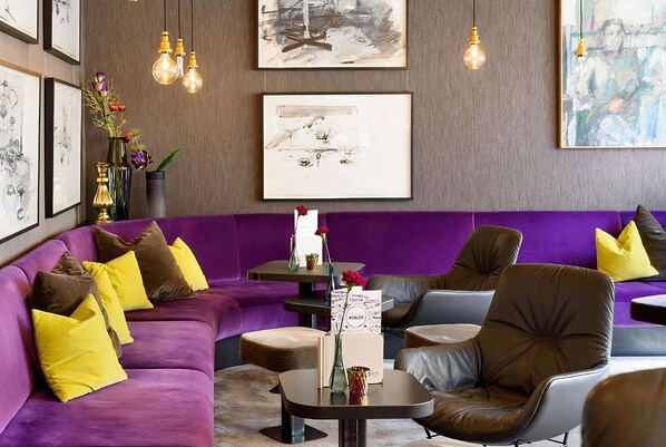 A modern lounge area with a purple sofa, leather chairs, and artwork on the walls.
