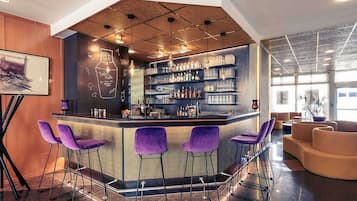 A bar area with a curved counter, bar stools, and shelves stocked with bottles and glasses.
