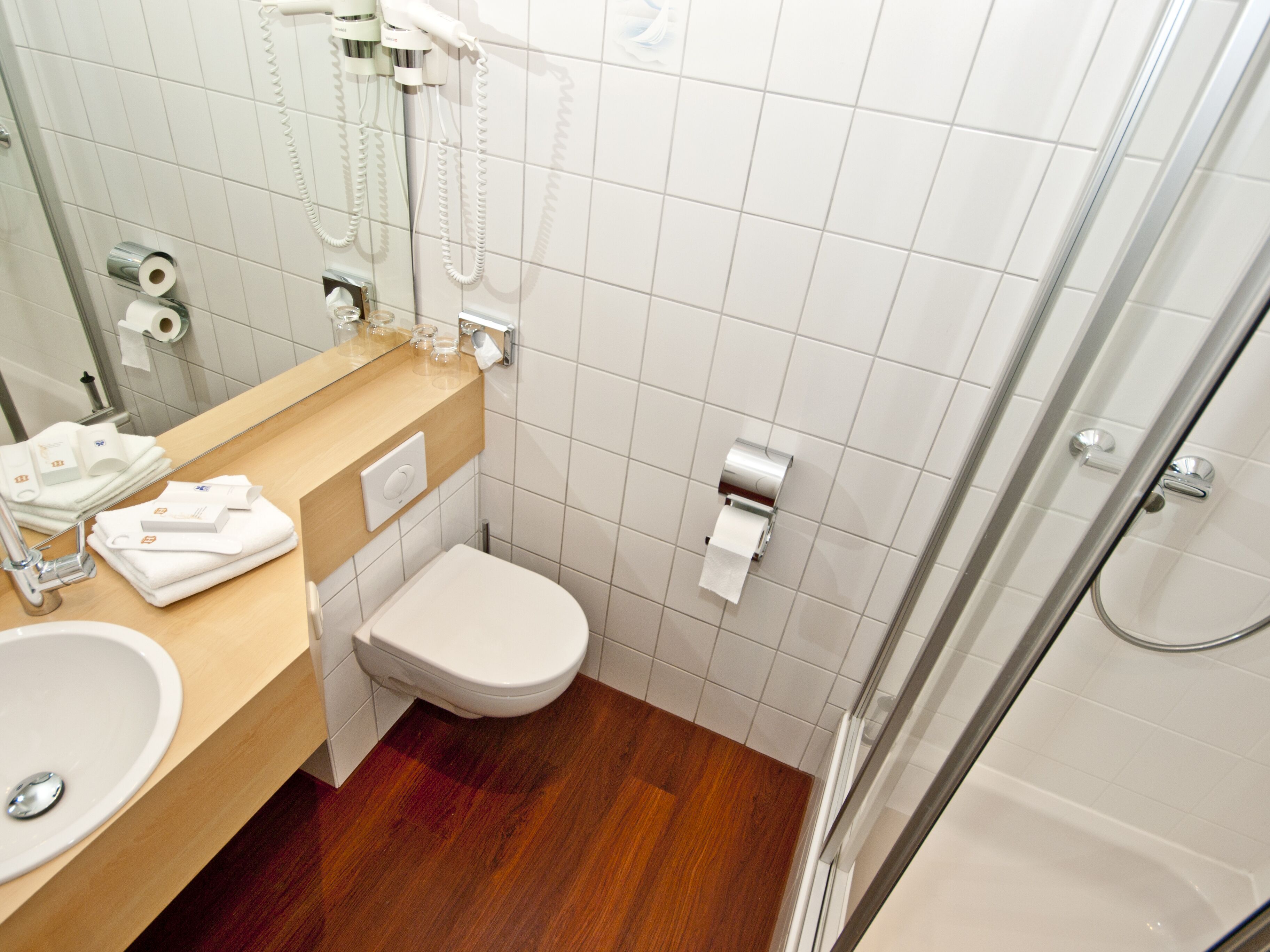 A modern bathroom with a wooden vanity, a white toilet, a glass shower enclosure, and a mirror.