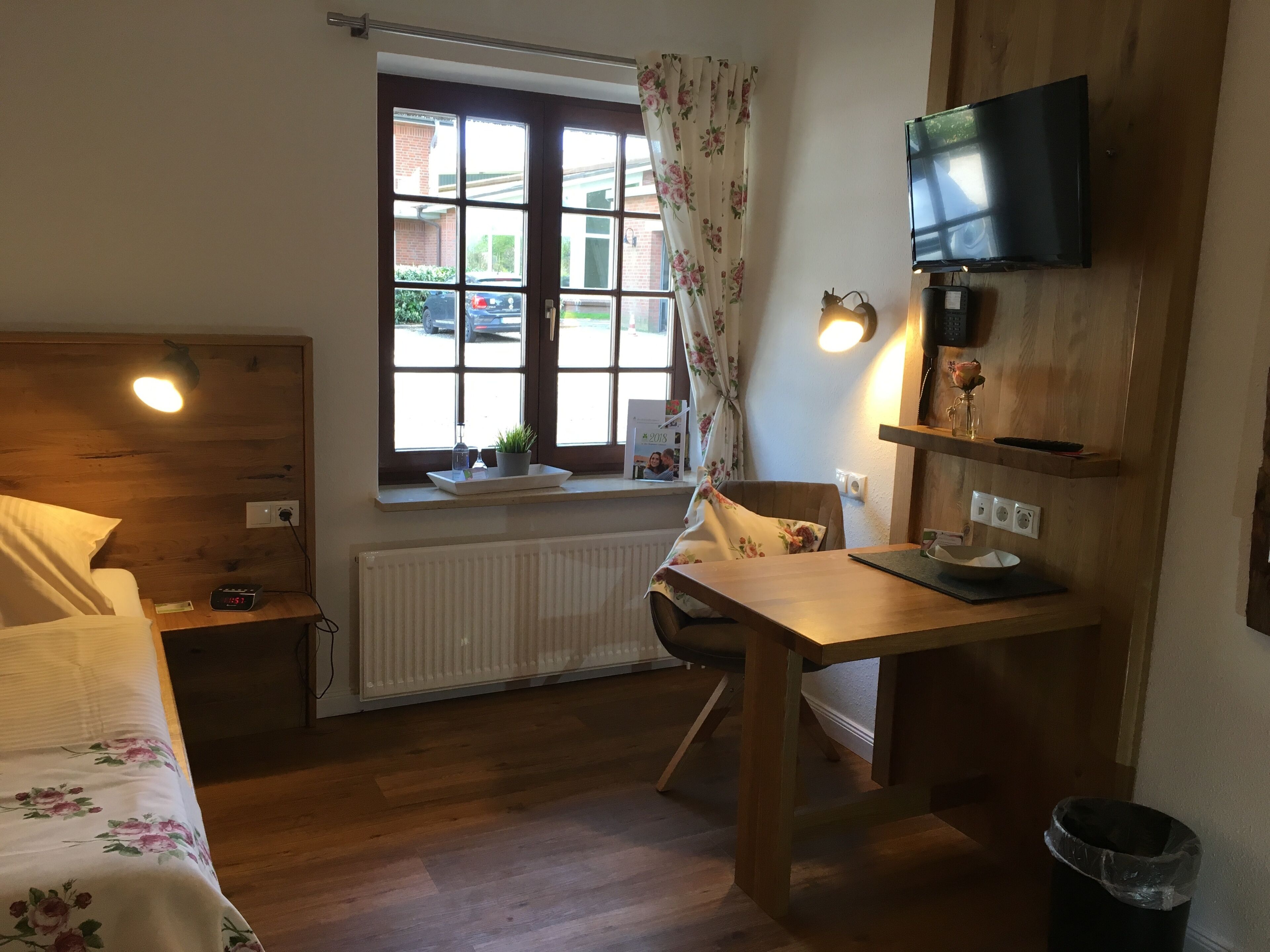A room with a bed, a desk, a chair, a TV, a window with curtains, and a radiator.