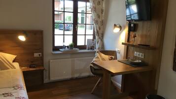A room with a bed, a desk, a chair, a TV, a window with curtains, and a radiator.