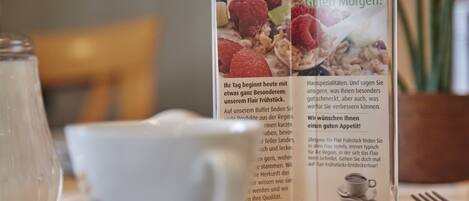Eine Speisekarte mit Text und Abbildungen von Speisen, platziert auf einem Tisch mit Tasse und Untertasse.