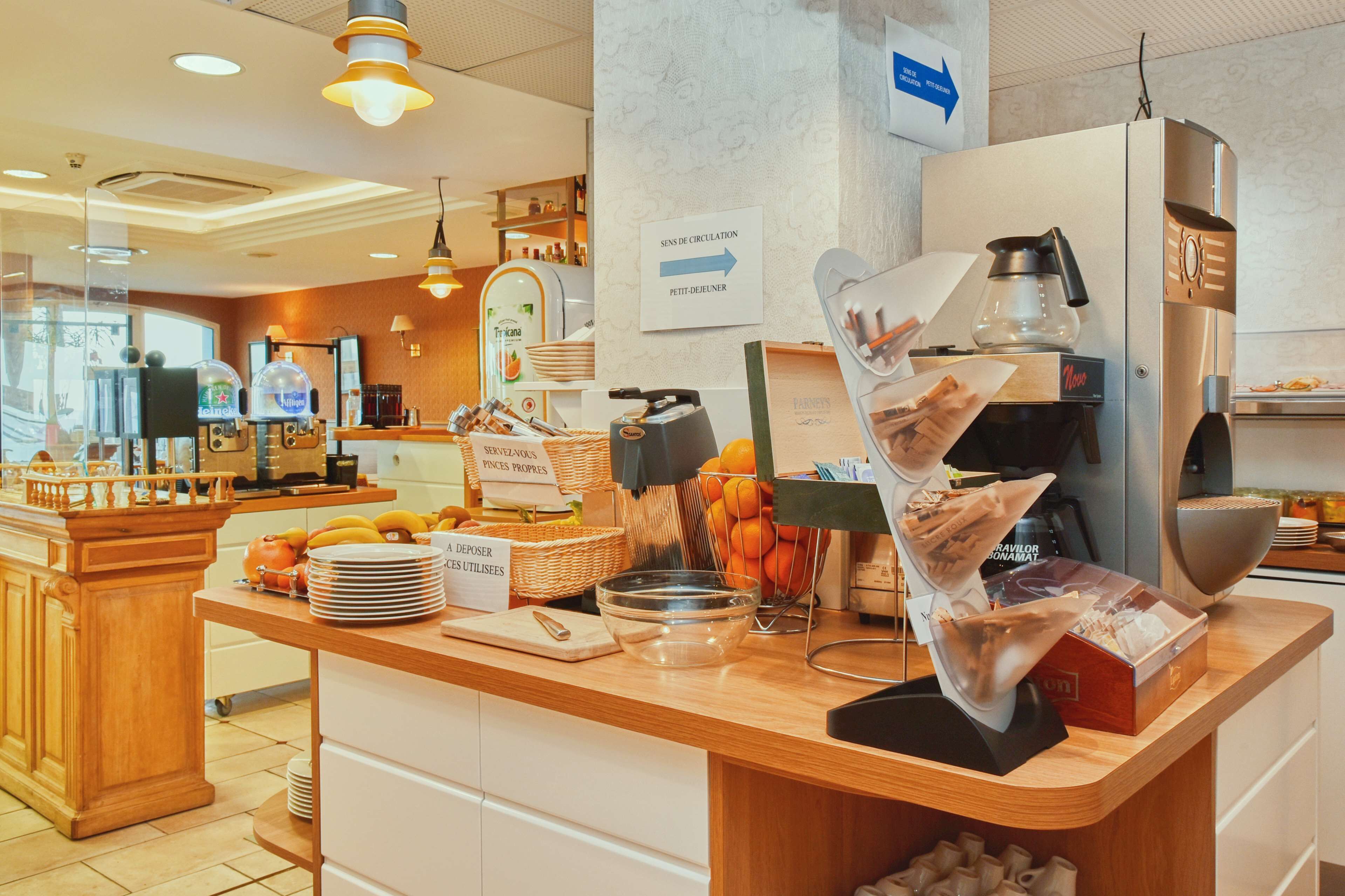 Un comptoir pour le petit-déjeuner équipé d’une machine à café, de fruits et d’un panneau indiquant une zone de passage.