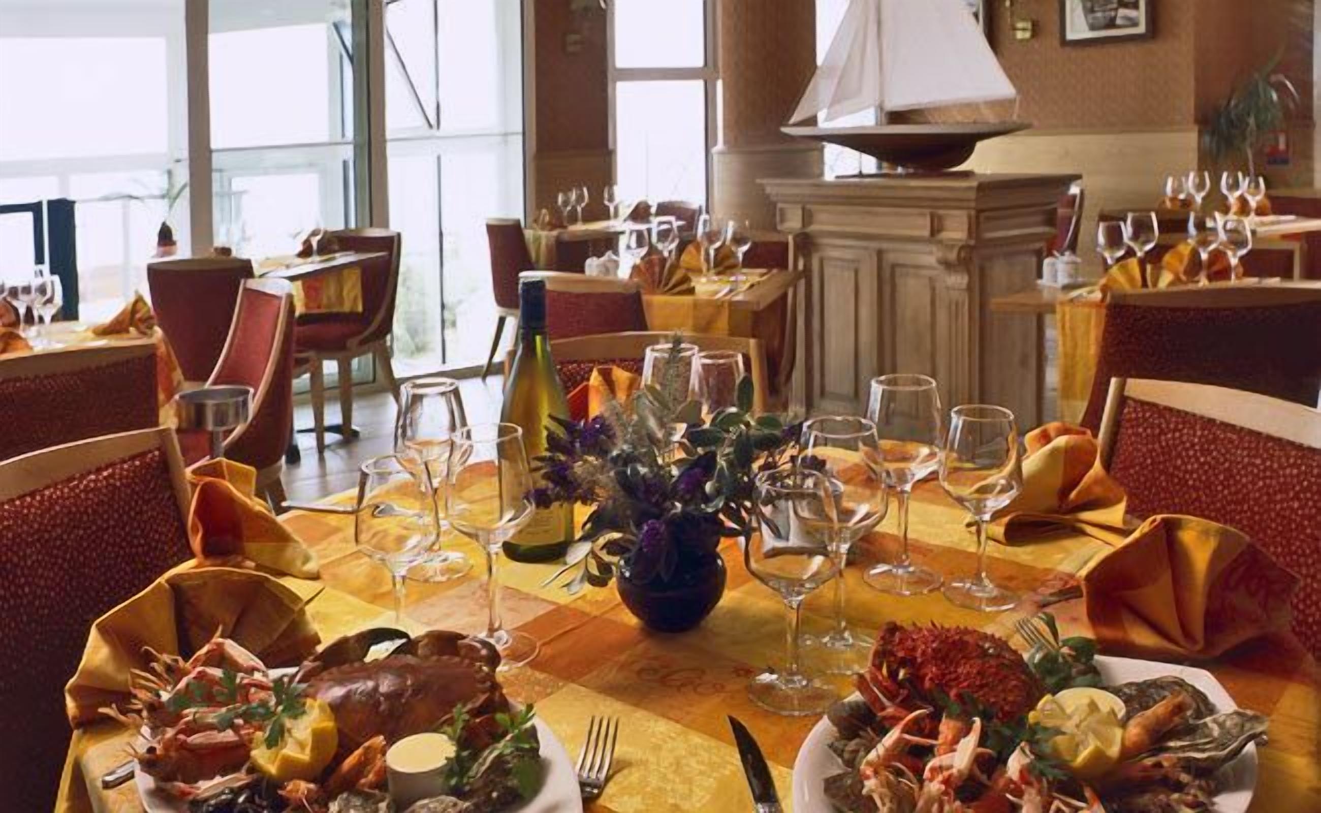 A restaurant setting with multiple tables, each set with wine glasses, plates of seafood, and a vase with flowers.