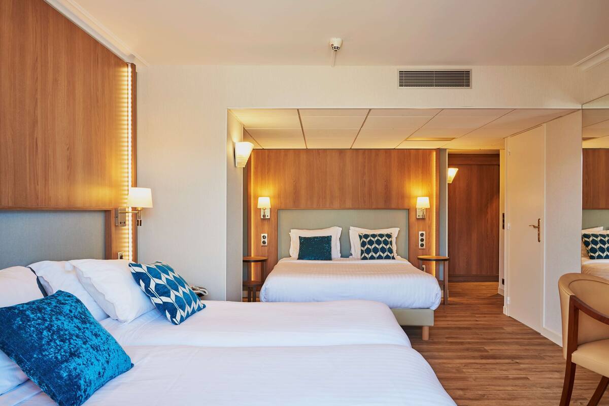 A hotel room with two beds, wooden headboards, bedside lamps, and a wooden floor.