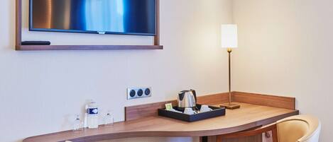Habitación de hotel con televisor de pantalla plana montado en la pared, una mesa con sillas, una lámpara y una bandeja con tazas y una tetera.
