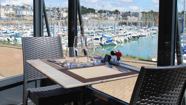 A dining table with chairs, a view of a marina with boats, and a cityscape in the background. - ibis Granville Port de plaisance (Granville)