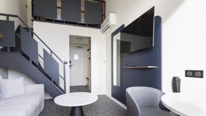 A modern hotel room with a staircase, a round table, a grey sofa, and a large mirror. - ibis Granville Port de plaisance (Granville)