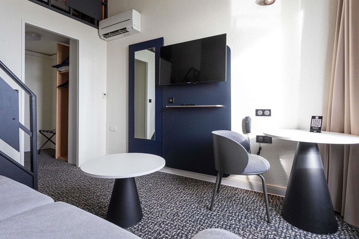 Una sala moderna con un sofá, una mesa redonda, una silla y un televisor montado en una puerta azul oscuro.