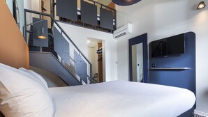 A hotel room with a bed, a staircase, an air conditioning unit, a TV, and a door. - ibis Granville Port de plaisance (Granville)