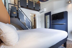 Quarto de hotel com cama, escada, ar condicionado, televisão e porta.