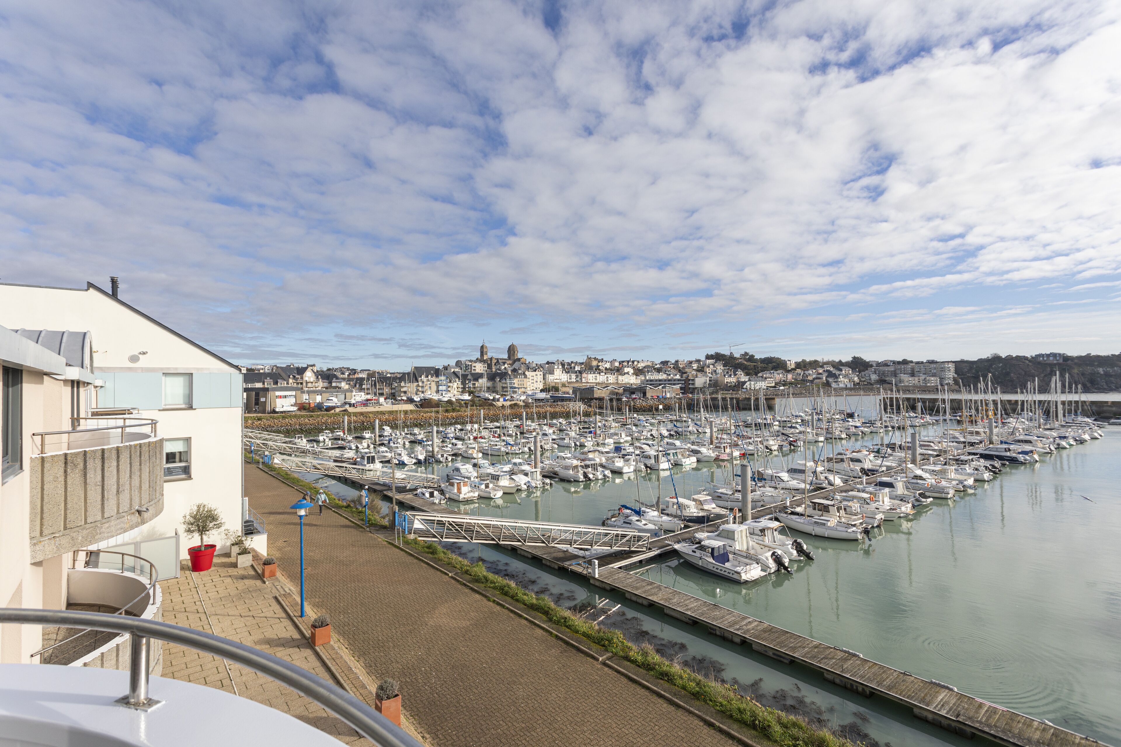 Un port de plaisance où sont amarrés de nombreux bateaux, un pont piétonnier et, au loin, une vue sur la ville.