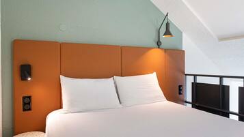 Uma cama com roupa branca, cabeceira e mesa de cabeceira com abajur.
