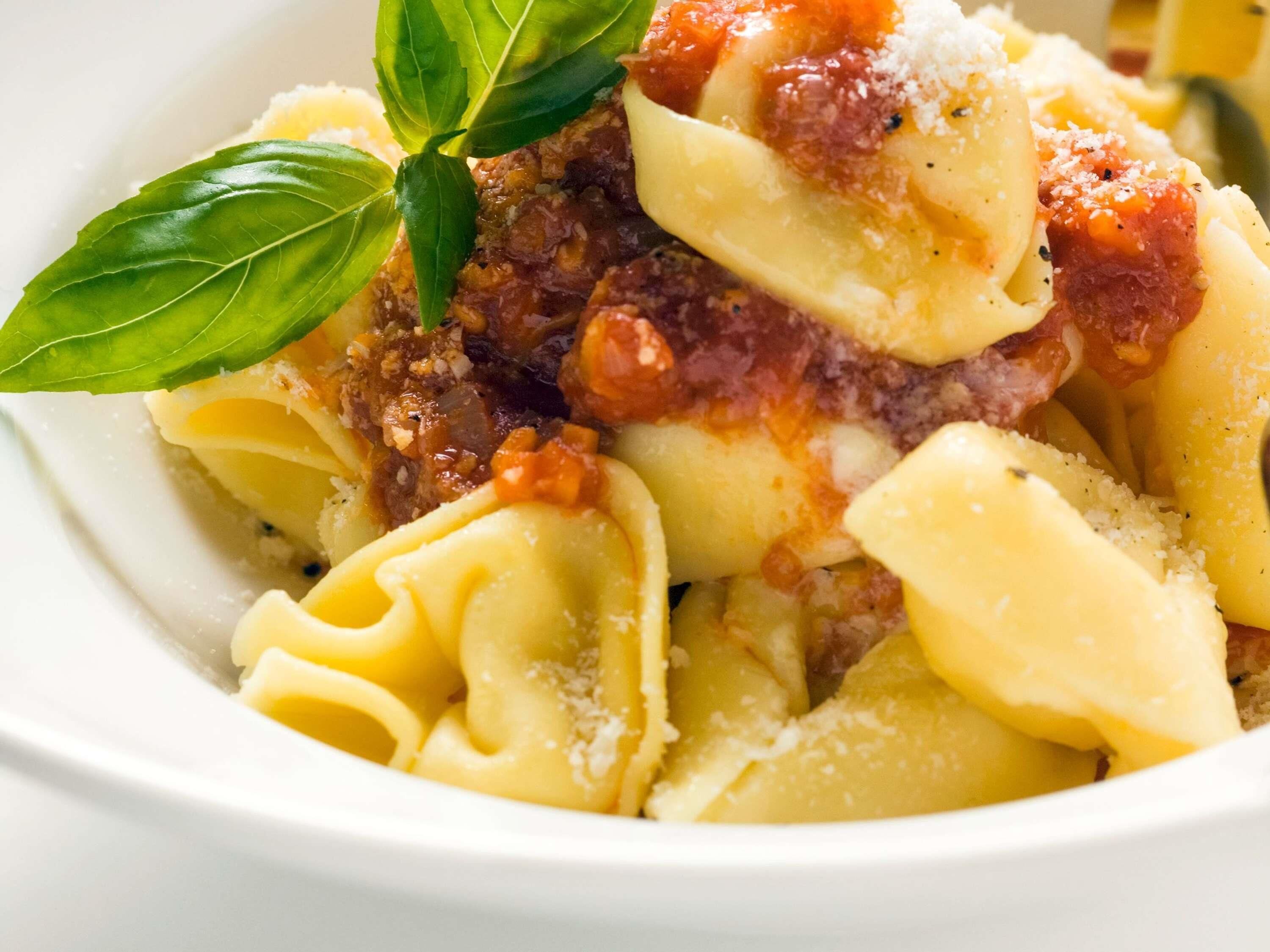 A bowl of pasta with a tomato-based sauce, garnished with basil and grated cheese.